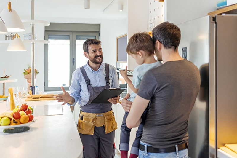 Technician speaking with a father holding his young son in their kitchen.