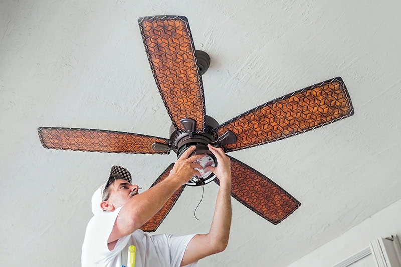 Whole-House Fans vs. Attic Fans. Photo of a technician installing a ceiling fan.