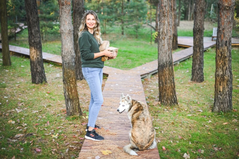 Woman carrying firewood on a trail in the woods with her dog.