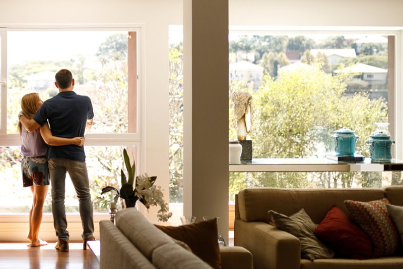 Couple in their living room looking out the living room window while hugging.