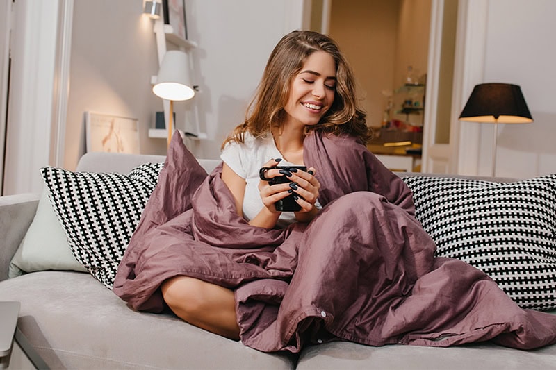 Maintaining the Best Humidity Level in a Maryland Winter. Photo of a woman wrapped in a blanket on her couch, drinking a hot beverage.